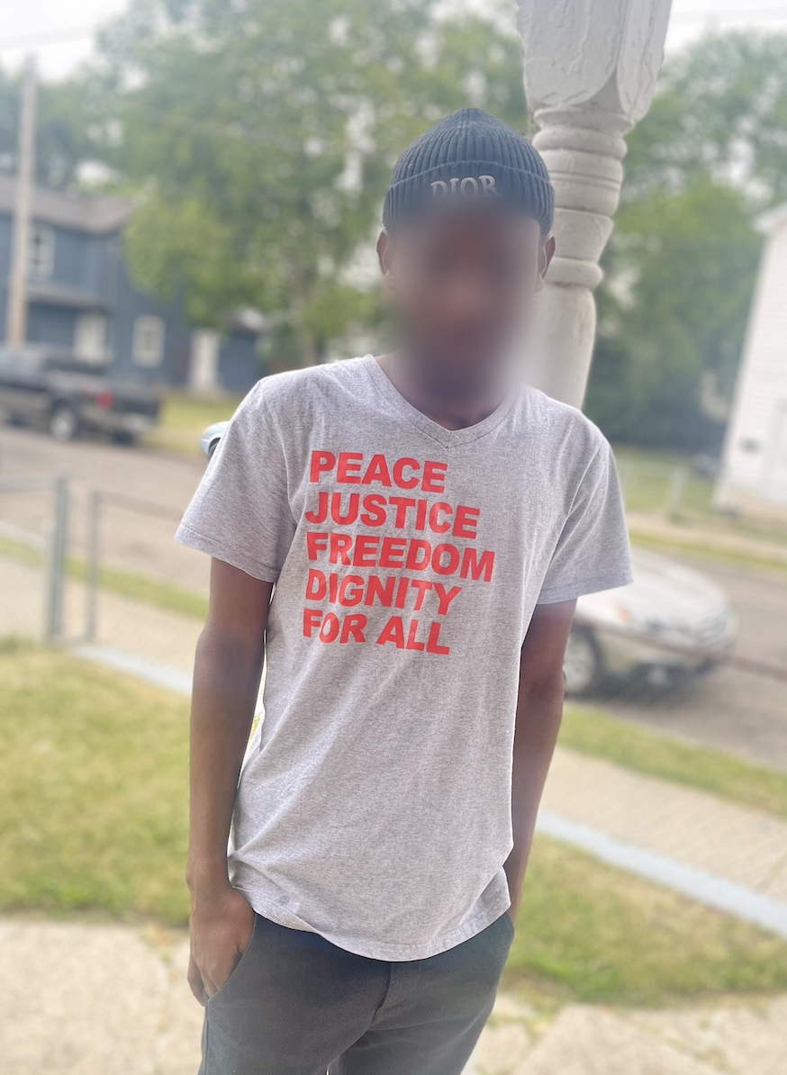 A man stands outside a home in Hamilton, Ohio, wearing a shirt he got from ICE as he was released from custody. He and hundreds like him are preparing to file for asylum in the US due to apartheid and slavery in Mauritania. (Photo credit: Ohio Immigrant Alliance © 2023)