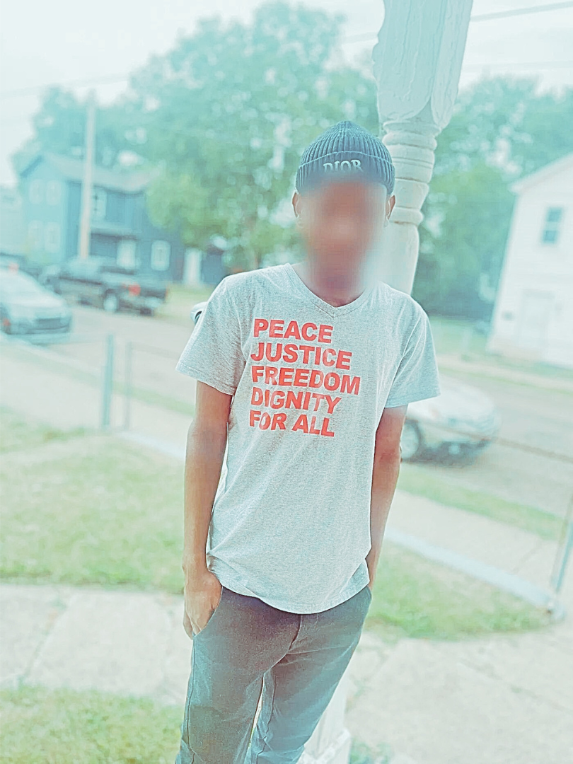 A young man wears a t-shirt that says "Peace, Justice, Freedom, and Dignity for All"