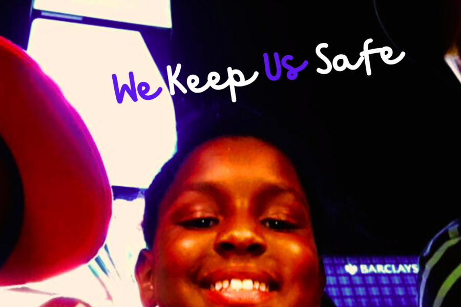 A Black boy wearing a red baseball hat is on the left, with another Black young boy smiling in the middle and a Black man wearing a green striped shirt looks on from the right. Two AAPI individuals appear in the background. The words say, in cursive, "We Keep Us Safe."