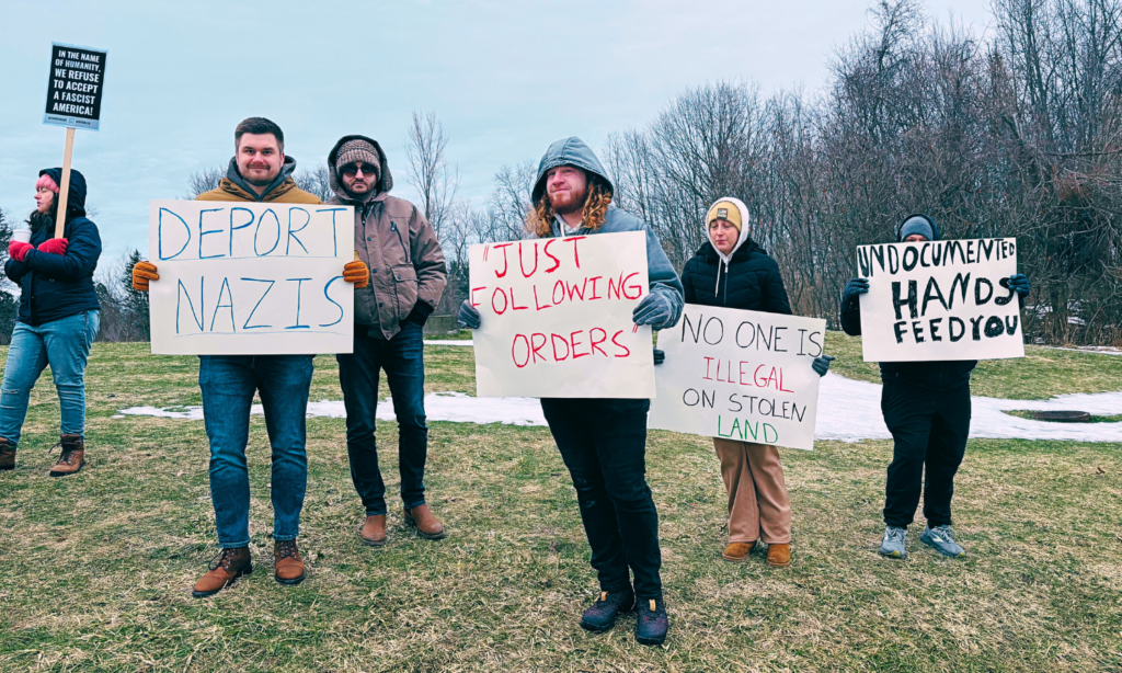 A group of people face the camera holding signs that decry Nazism and support immigrants