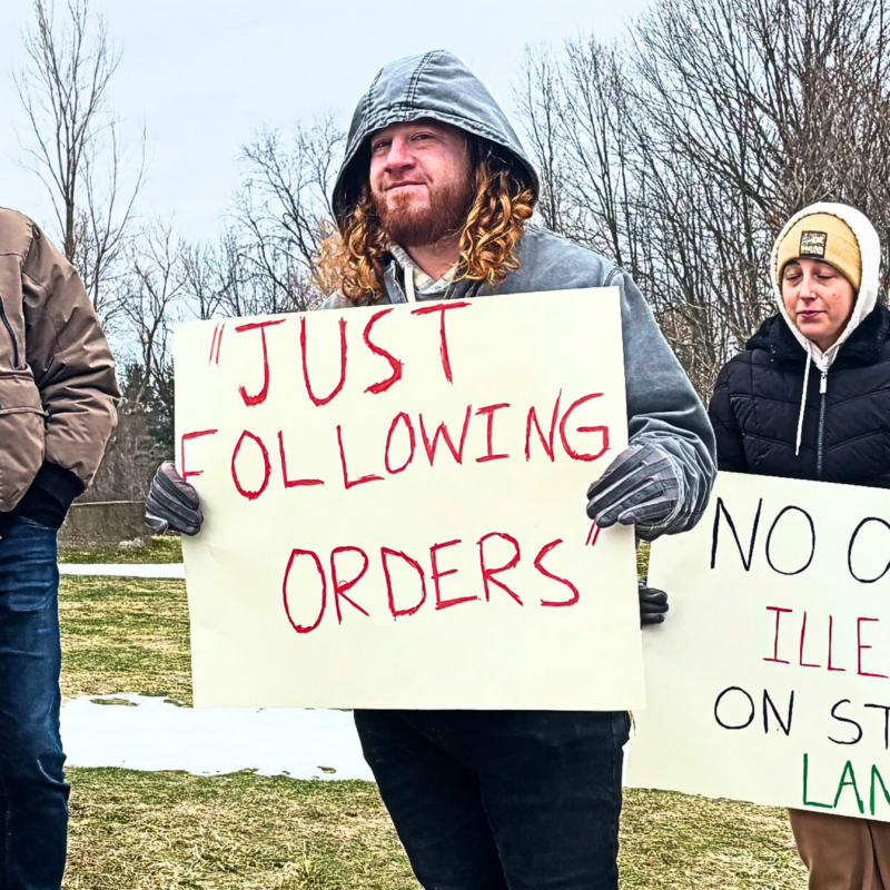 A group of people face the camera holding signs that decry Nazism and support immigrants