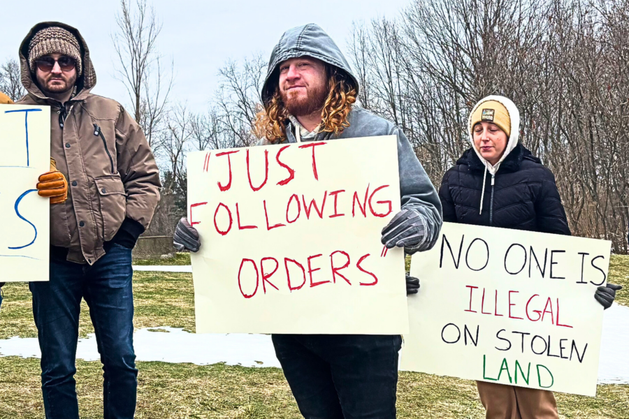 A group of people face the camera holding signs that decry Nazism and support immigrants