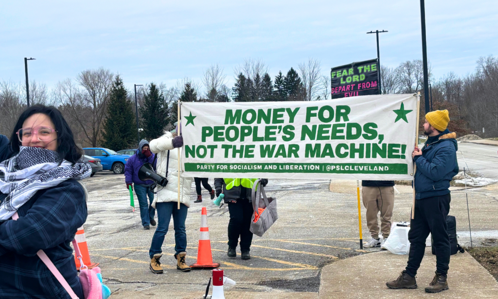 A crowd holds a large banner with green letters